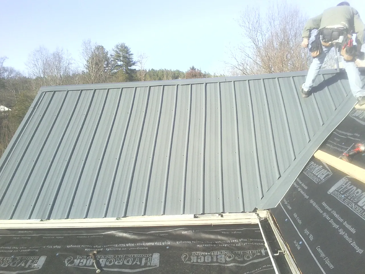 Crew installing dark green standing seam panels over synthetic underlayment in Watson