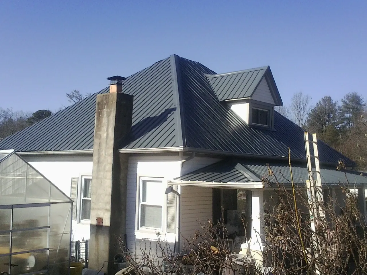Dark blue standing seam metal roof on a white farmhouse with dormer — Slate & Tile Roof Repair by Roofing Brothers in Watson