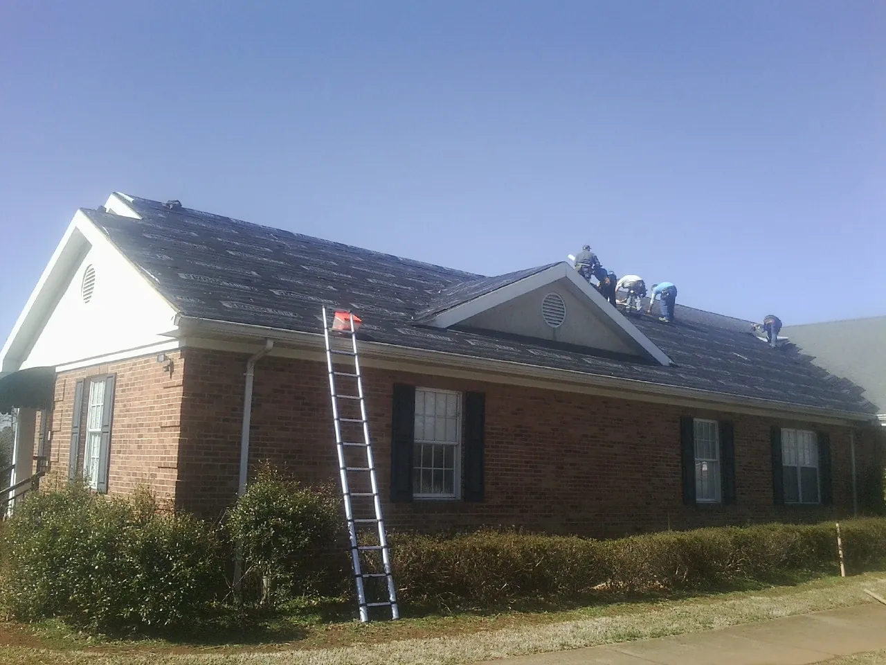 Crew tearing shingles off a brick ranch roof with a ladder set — Metal Roof Repair work by our crew in Watson